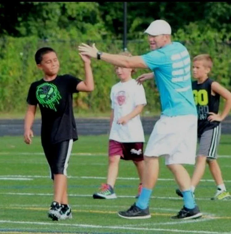 A coach high-fiving a young athlete on the field